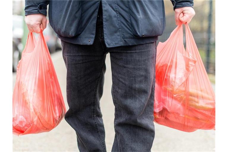 Ein Mann trägt seine Einkäufe in Plastiktüten nach Hause. Ab Januar 2022 sind Plastiktüten an Ladenkassen in Deutschland verboten. Foto: Sebastian Gollnow/dpa