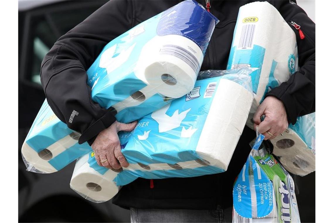 Ein Mann trägt Toilettenpapier und Küchenrollen aus einem Supermarkt. Foto: Rene Traut/dpa