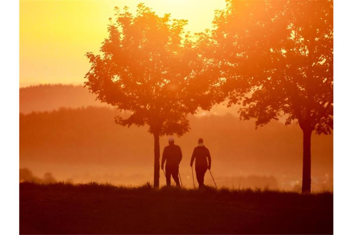 Ein Mann und eine Frau gehen im Gegenlicht der Morgensonne spazieren. Foto: Thomas Warnack/dpa/Archivbild
