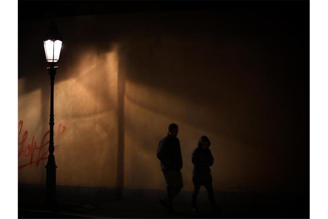 Ein Mann und eine Frau gehen zu nächtlicher Stunde im Licht einer Straßenlaterne auf dem Gehweg. Foto: Hildenbrand/Archivbild