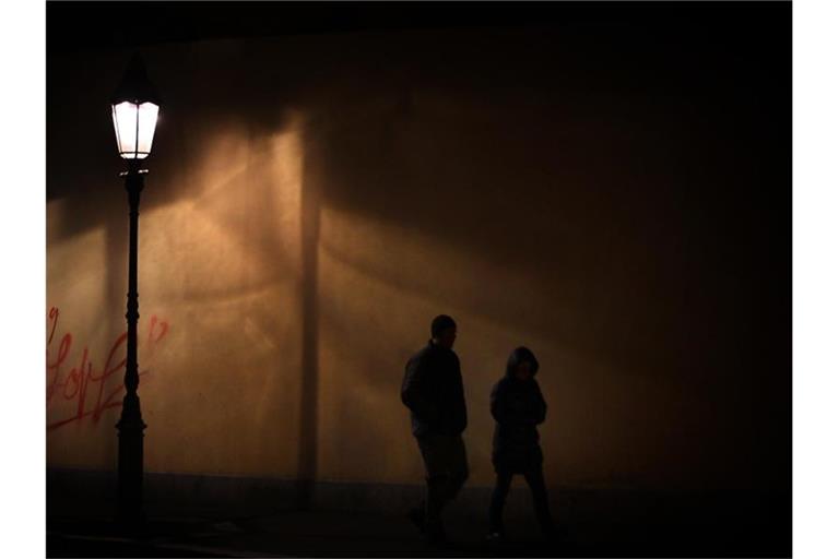 Ein Mann und eine Frau gehen zu nächtlicher Stunde im Licht einer Straßenlaterne auf dem Gehweg. Foto: Hildenbrand/Archivbild