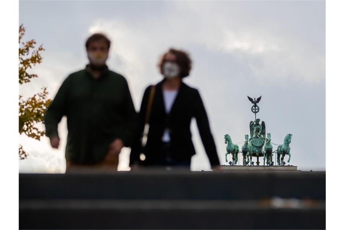 Ein Mann und eine Frau mit Mund-Nasen-Schutz vor der Quadriga des Brandenburger Tores in Berlin. Foto: Christoph Soeder/dpa