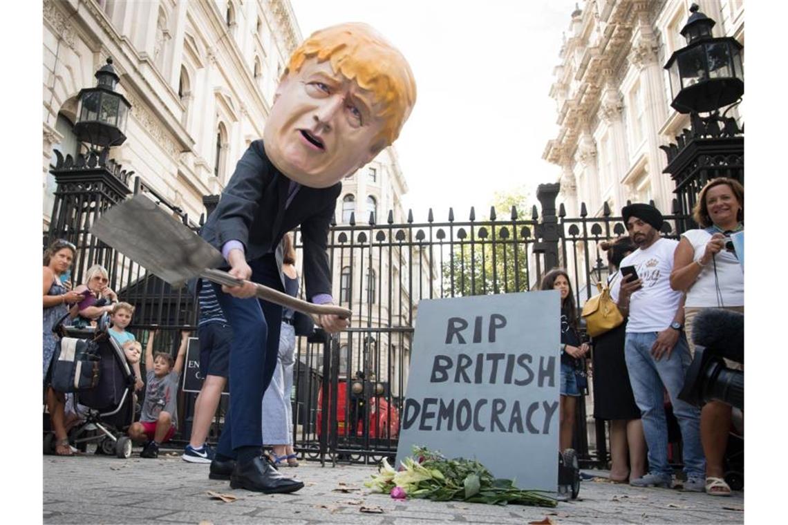 Johnson verordnet britischem Parlament eine Zwangspause Ein Mann verkleidet mit einem riesigen Kopf des britischen Premierministers Johnson neben einem symbolischen Grabstein mit der Aufschrift „RIP British Democracy“ (Ruhe in Frieden britische Demokratie). Foto: Stefan Rousseau/PA Wire