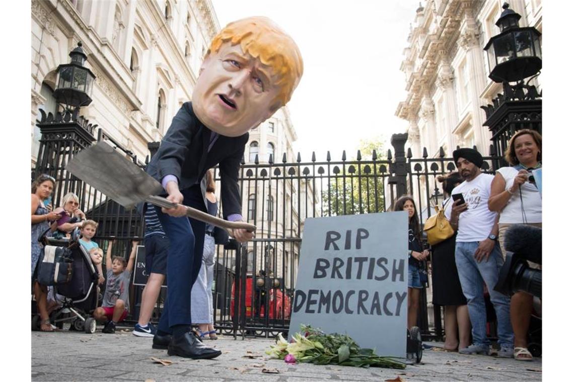 Ein Mann verkleidet mit einem riesigen Kopf des britischen Premierministers Johnson neben einem symbolischen Grabstein mit der Aufschrift „RIP British Democracy“ (Ruhe in Frieden britische Demokratie). Foto: Stefan Rousseau/PA Wire