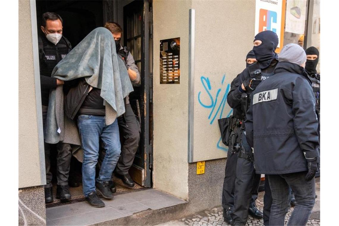 Ein Mann wird bei einer Razzia, mit einer Decke über dem Kopf, von der Polizei abgeführt. Foto: Christophe Gateau/dpa