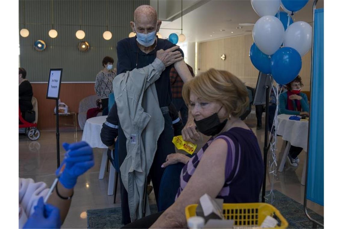 Ein Mann zieht sein Hemd hoch, während seine Frau ihre vierte Dosis des Coronavirus-Impfstoffs in einem privaten Pflegeheim in Petah Tikva erhält. Foto: Ariel Schalit/AP/dpa