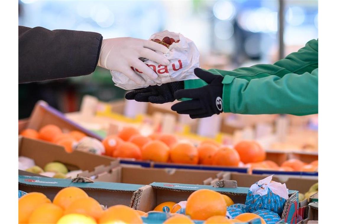 Ein Markthändler gibt mit Handschuhen eine Tüte an eine Kundin. Foto: Sebastian Gollnow/dpa/Symbolbild