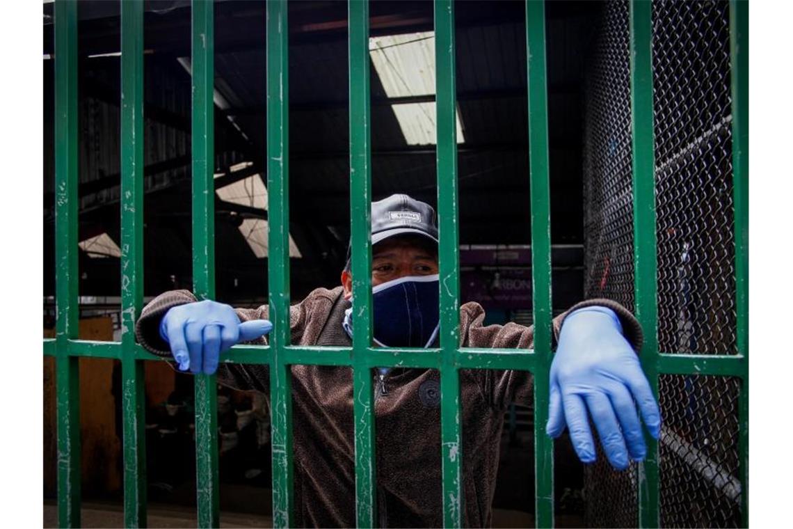 Ein Markthändler schaut im ecuadorianischen Quito durch eine Absperrung. Foto: Juan Diego Montenegro/dpa