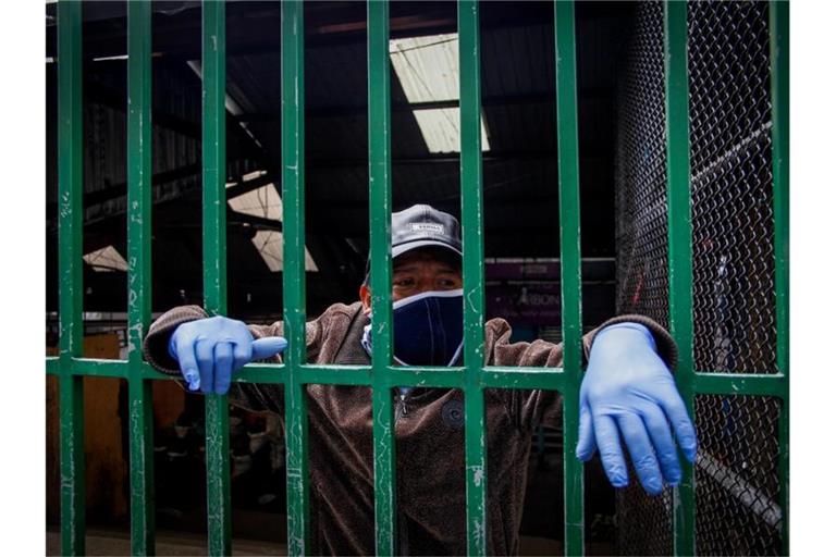 Ein Markthändler schaut im ecuadorianischen Quito durch eine Absperrung. Foto: Juan Diego Montenegro/dpa