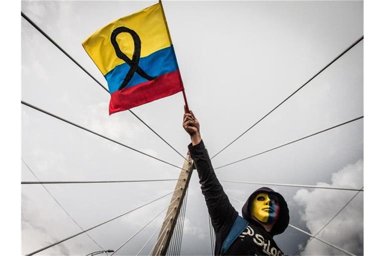 Ein maskierter Demonstrant schwenkt die kolumbianische Flagge. Foto: Juan Pablo Otalvaro M/dpa