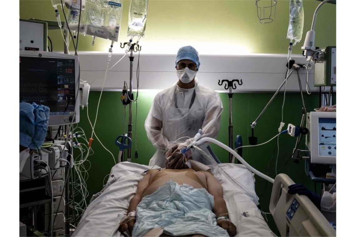 Ein medizinischer Angestellter (M) kümmert sich auf der Intensivstation eines Krankenhauses in Pierre-Benite um einen Corona-Patienten. Foto: Jeff Pachoud/AFP/dpa