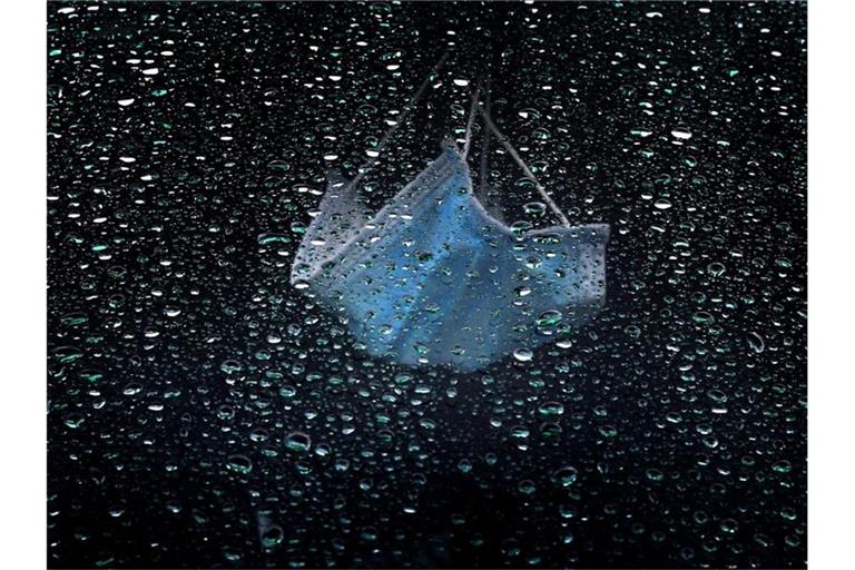 Ein medizinischer Mundschutz hängt am Rückspiegel eines im Regen parkenden Autos. Foto: Karl-Josef Hildenbrand/dpa/Symbolbild/Archiv