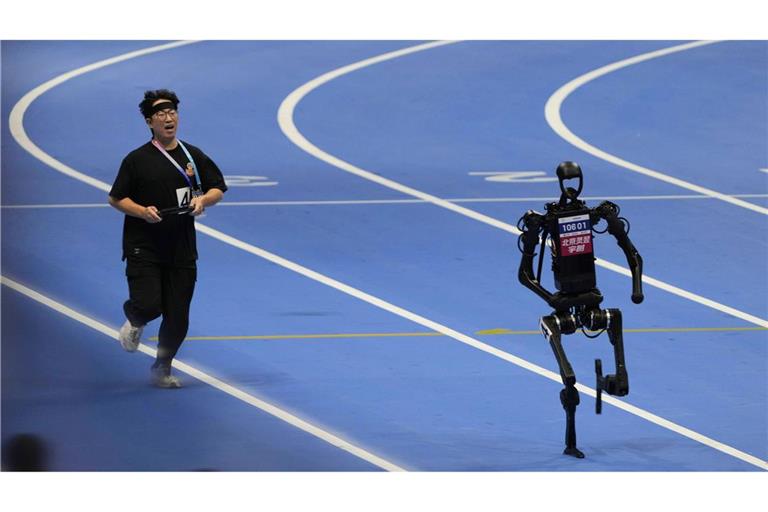 Ein menschlicher Bediener versucht, mit einem Roboter im 1500-Meter-Lauf bei den World Humanoid Robot Games in Peking Schritt zu halten.