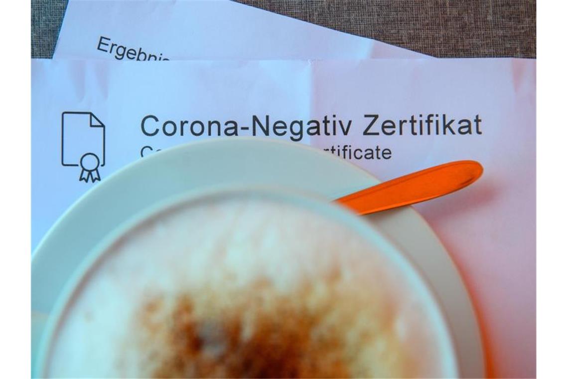 Ein Milchkaffee steht in einem Café auf einem Tisch auf einem Corona-Negativ Zertifikat. Foto: Klaus-Dietmar Gabbert/dpa-Zentralbild/dpa/Symbolbild