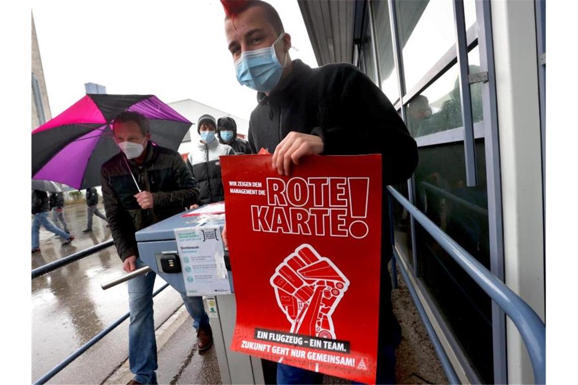 Ein Mitarbeiter der Airbus-Tochter Premium Aerotec verlässt nach einer Protestaktion mit einem Plakat, auf dem "Wir zeigen dem Management die rote Karte" zu lesen ist, das Betriebsgelände des Unternehmens. Foto: Karl-Josef Hildenbrand/dpa