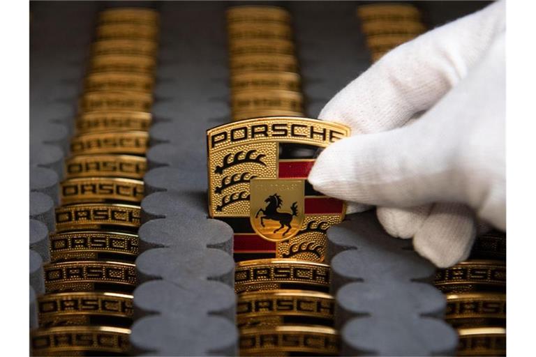 Ein Mitarbeiter der Porsche AG zeigt in der Produktion Porsche-Wappen. Foto: Marijan Murat/dpa/Archivbild