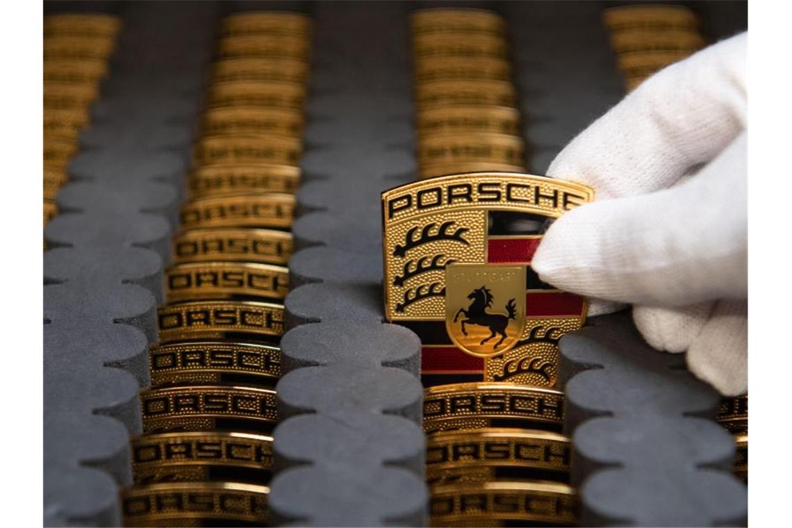 Ein Mitarbeiter der Porsche AG zeigt in der Produktion Porsche-Wappen. Foto: Marijan Murat/dpa/Symbolbild