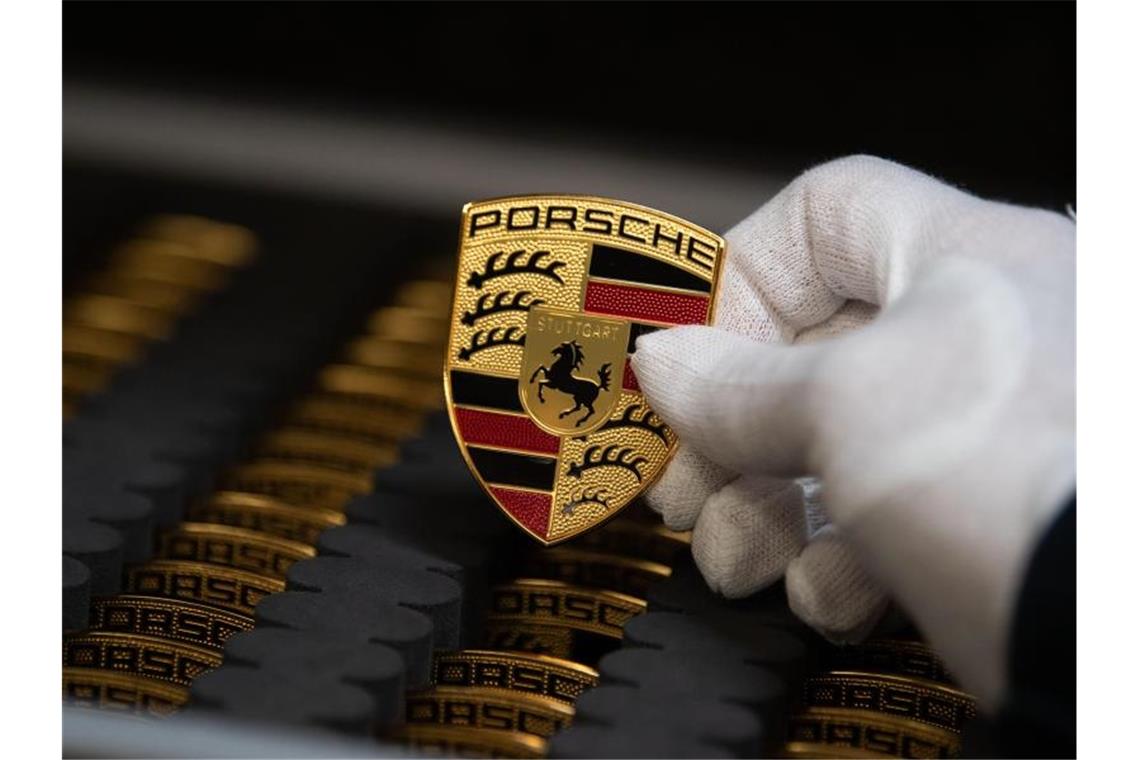 Ein Mitarbeiter der Porsche AG zeigt in der Produktion Porsche-Wappen. Foto: Marijan Murat/dpa/Archivbild