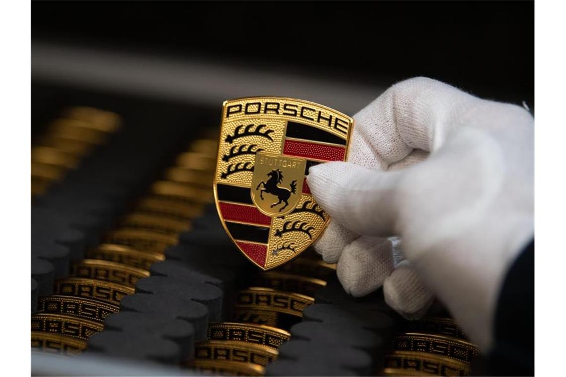 Ein Mitarbeiter der Porsche AG zeigt in der Produktion Porsche-Wappen. Foto: Marijan Murat/dpa/Archivbild