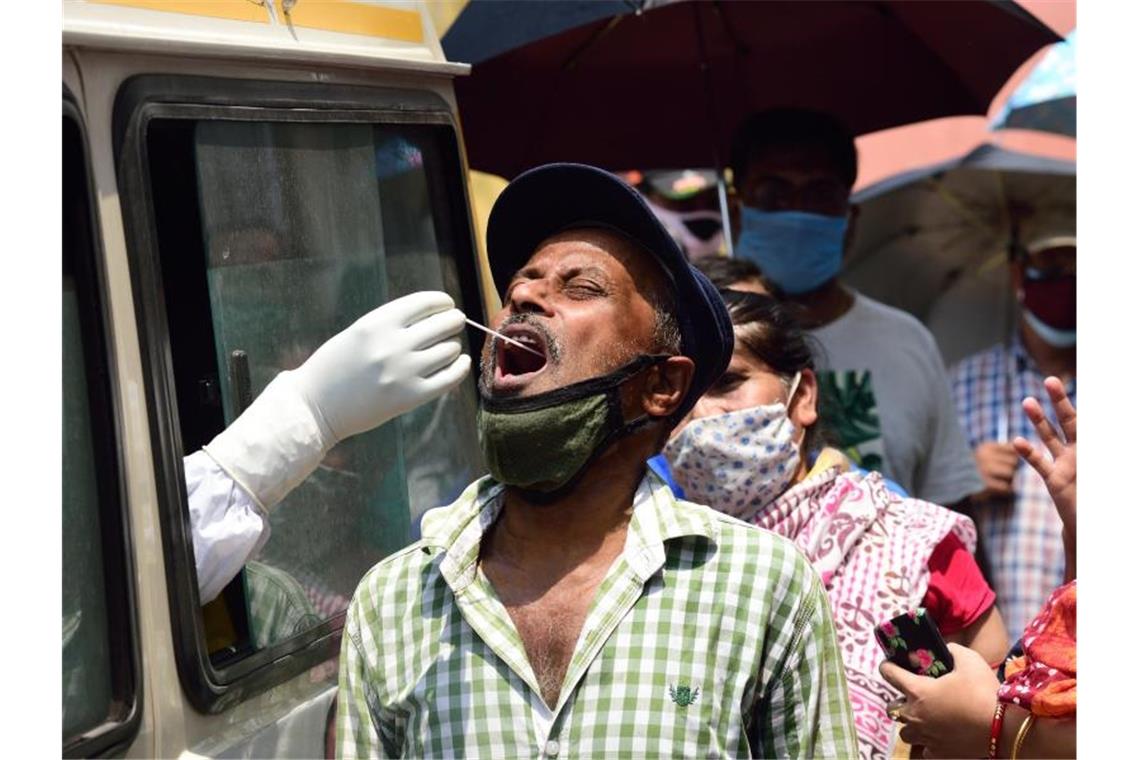 Ein Mitarbeiter des Gesundheitswesens entnimmt in Kalkutta aus einem Auto heraus einen Abstrich für einen Corona-Test. Foto: Sumit Sanyal/SOPA Images via ZUMA Wire/dpa