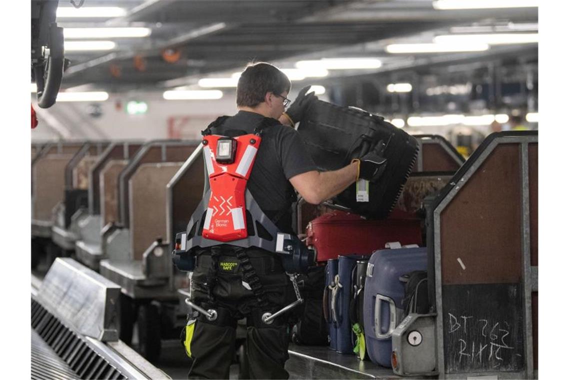 Exoskelette sollen Schwerstarbeit erleichtern Ein Mitarbeiter des Stuttgarter Flughafens hebt mit Unterstützung eines Exoskeletts einen Koffer auf einen Gepäckwagen. Foto: Marijan Murat/dpa