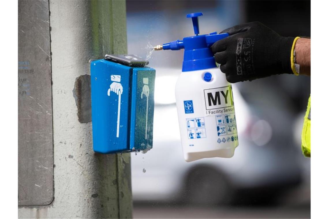 Corona: Reinigungsfirmen leiden unter weniger Aufträgen Ein Mitarbeiter einer Reinigungsfirma den Drücker einer Ampel. Foto: Marijan Murat/dpa/Archivbild
