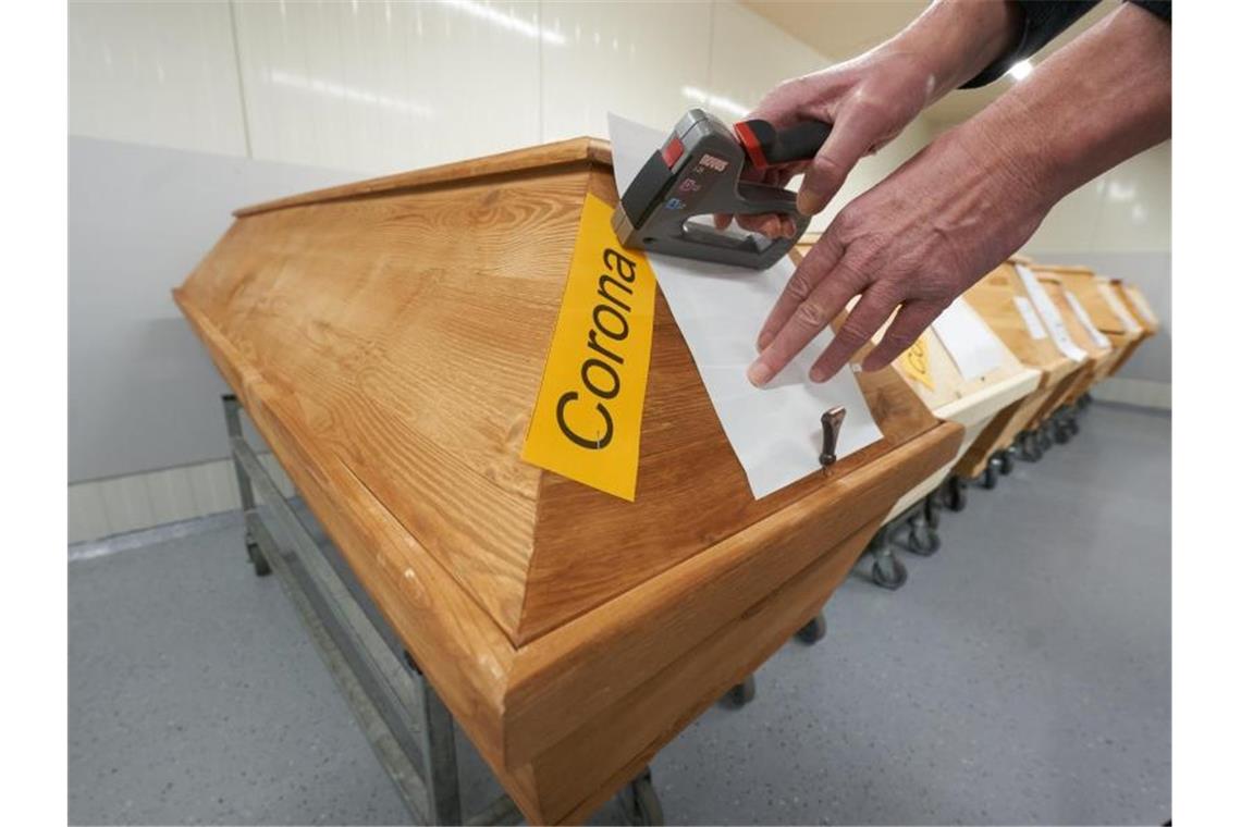 Fast 900 neue Corona-Tote Ein Mitarbeiter eines Krematoriums in Rheinland-Pfalz bringt an einem Sarg die Markierung „Corona“ an. Foto: Thomas Frey/dpa