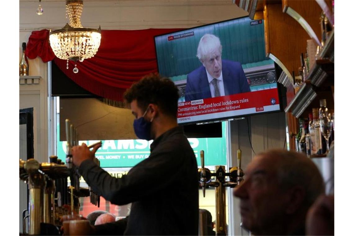 Ein Mitarbeiter eines Liverpooler Pubs schenkt Bier ein, während Premierminister Johnson im Hintergrund das neue Drei-Stufen-System erklärt. Foto: Peter Byrne/PA Wire/dpa