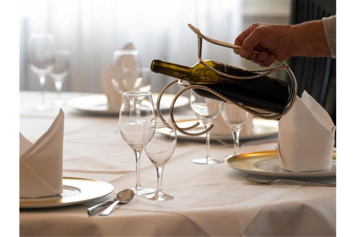 Ein Mitarbeiter eines Restaurants schenkt an einem gedeckten Tisch Wein ein. Foto: Bernd Weißbrod/dpa/Archivbild