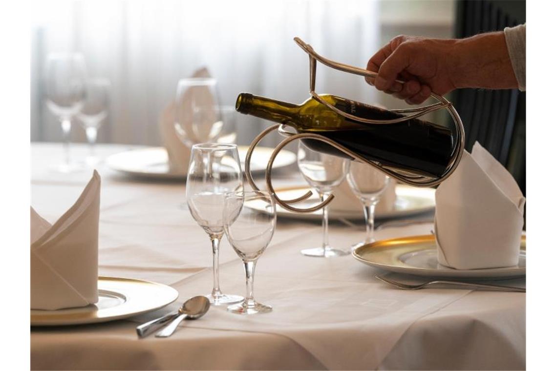 Lage im Gastgewerbe weiter schwierig: Arbeitskräfte fehlen Ein Mitarbeiter eines Restaurants schenkt an einem gedeckten Tisch Wein ein. Foto: Bernd Weißbrod/dpa/Archivbild