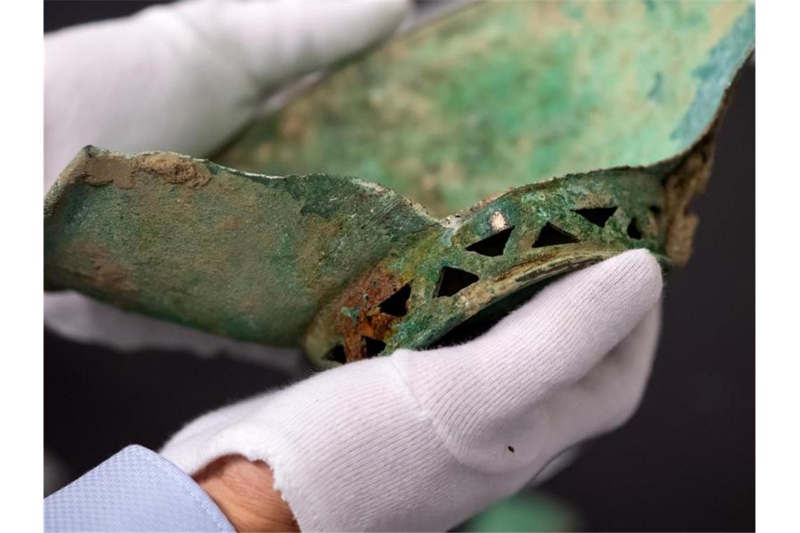 Reitergrab und Hinweis auf römische Siedlung entdeckt Ein Mitarbeiter hält eine Schale aus Bronze in den Händen. Foto: Sven Hoppe/dpa