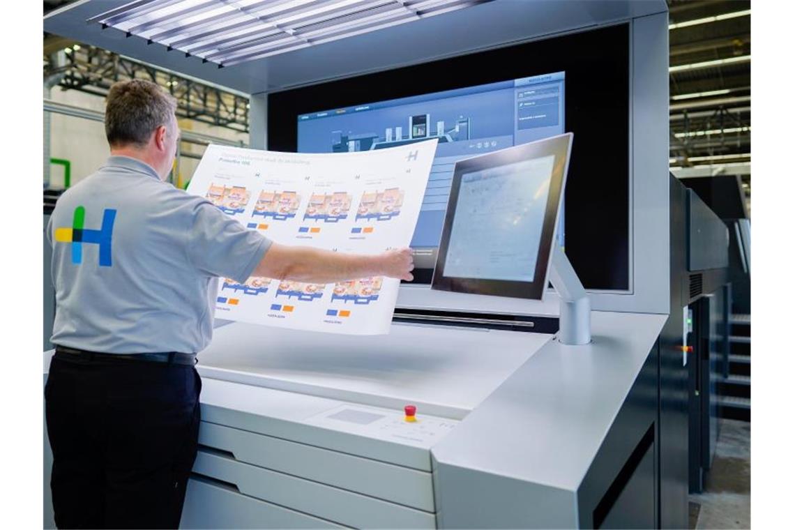 Ein Mitarbeiter hält in einer Werkshalle am Stammsitz der Heidelberger Druckmaschinen AG an einer Digitaldruckmaschine vom Typ „Primefire“ einen bedruckten Bogen in den Händen. Foto: Uwe Anspach/dpa