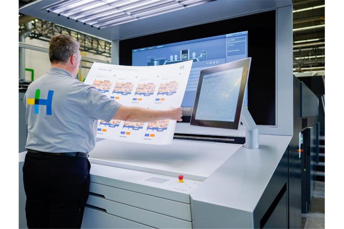 Ein Mitarbeiter hält in einer Werkshalle am Stammsitz der Heidelberger Druckmaschinen AG an einer Digitaldruckmaschine einen bedruckten Bogen in den Händen, auf dem Verpackungsmuster zu sehen sind. Foto: Uwe Anspach/dpa/Archivbild