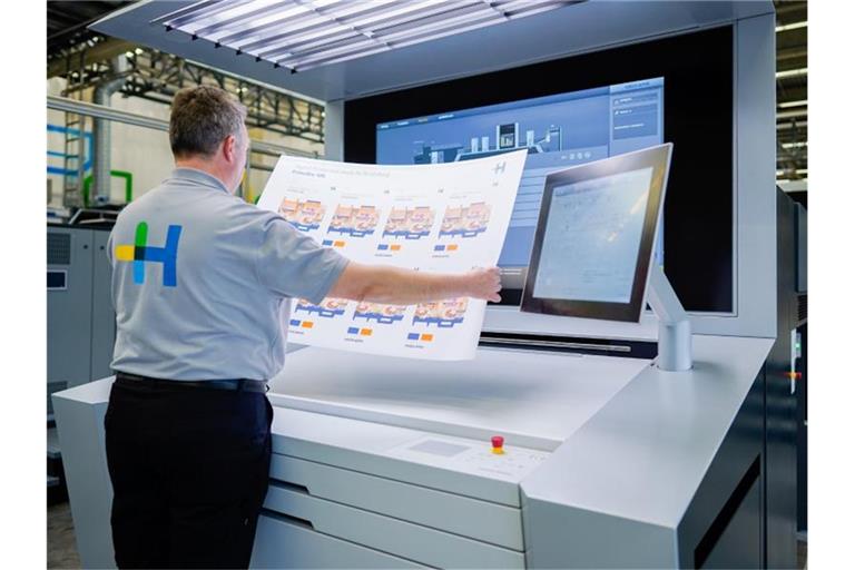 Ein Mitarbeiter hält in einer Werkshalle der Heidelberger Druckmaschinen AG an einer Digitaldruckmaschine einen bedruckten Bogen in den Händen. Foto: Uwe Anspach/dpa