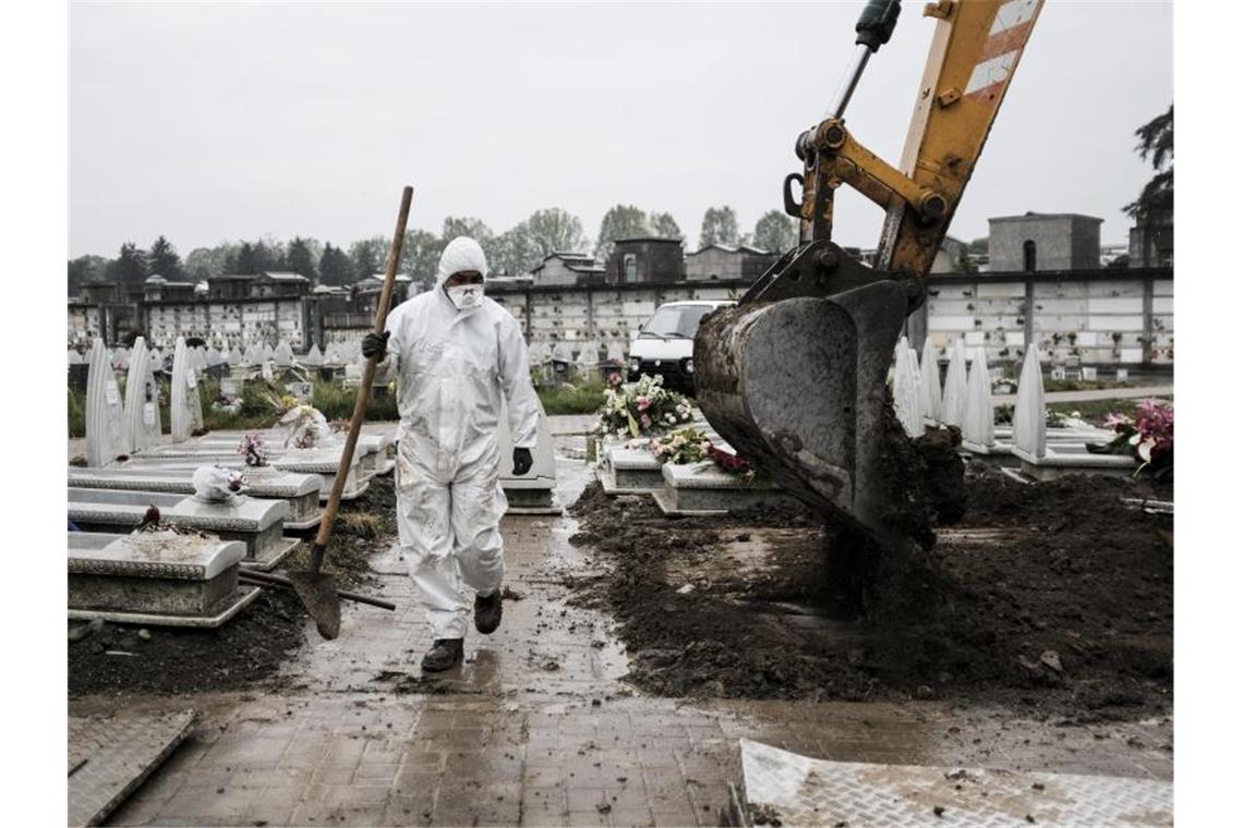 Ein Mitarbeiter im Schutzanzug geht in der Industriestadt Turin über einen Friedhof, auf dem frische Gräber ausgehoben werden. Foto: Marco Alpozzi/LaPresse via ZUMA Press/dpa