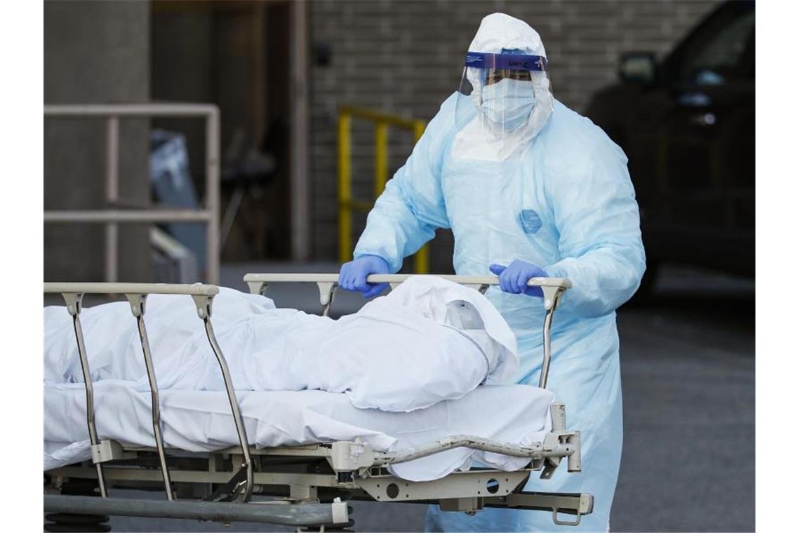 Ein Mitarbeiter in Schutzkleidung bringt eine Leiche zu einem Kühlanhänger, der als behelfsmäßige Leichenhalle im Wyckoff Heights Medical Center in New York dient. Foto: John Minchillo/AP/dpa