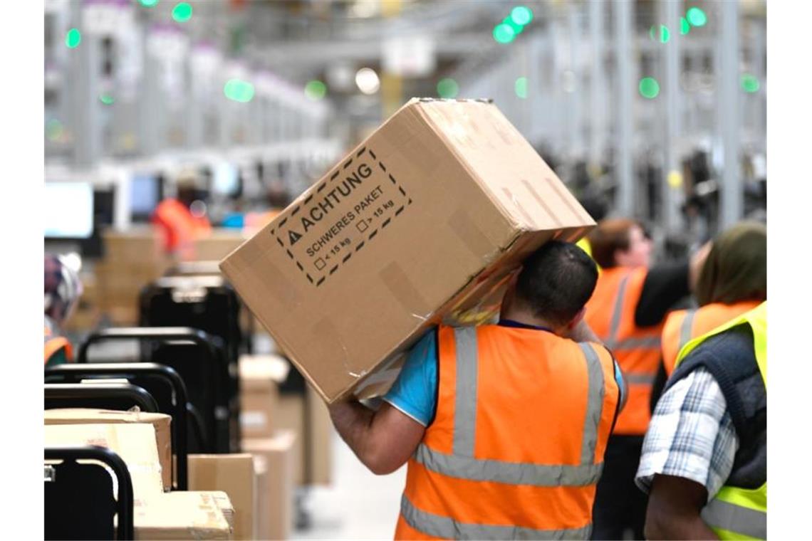 Ein Mitarbeiter trägt ein Paket im Logistikzentrum des Versandhändlers Amazon. Foto: Ina Fassbender/dpa