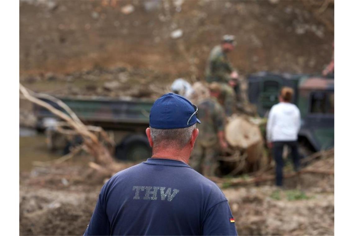 Ein Mitarbeiter vom Technischen Hilfswerk (THW) blickt zu Bundeswehrsoldaten hinüber. Foto: Thomas Frey/dpa