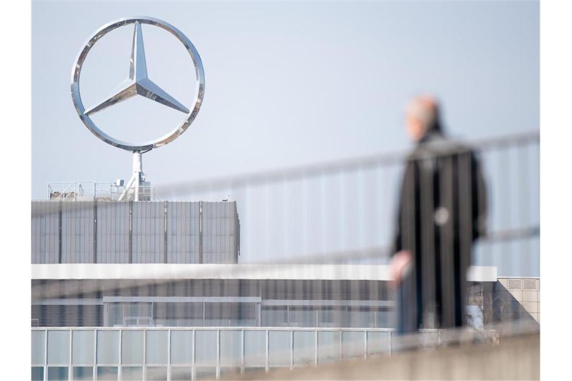 Ein Mitarbeiter von Daimler geht vor einem Mercedes-Stern Richtung Werk. Foto: Sebastian Gollnow/dpa