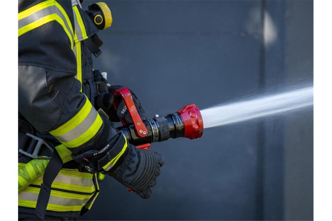 Ein Mitglied der Feuerwehr spritzt aus einem Schlauch mit Wasser. Foto: David Inderlied/dpa/Symbolbild