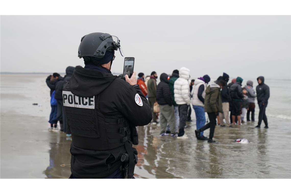 Ein Mitglied der französischen Behörden filmt eine Gruppe von Menschen, bei denen es sich vermutlich um Migranten handelt, die am Strand von Gravelines, Frankreich, warten, während sie versuchen, ein kleines Boot zu besteigen, um den Ärmelkanal zu überqueren.