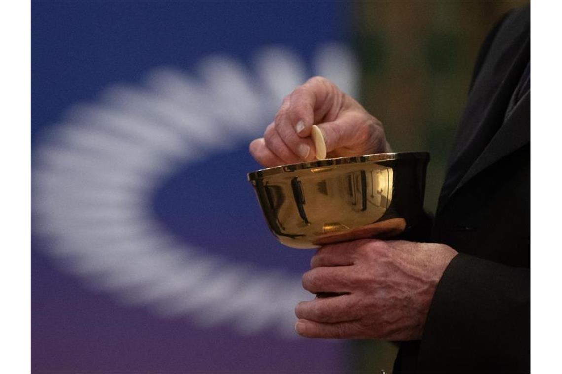 Ein Mitglied der Kirchengemeinde hält während eines Gottesdienstes mit Abendmahl im katholischen Dom St. Bartholomäus vor dem Logo des ÖKT eine Oblate in der Hand. Foto: Sebastian Gollnow/dpa