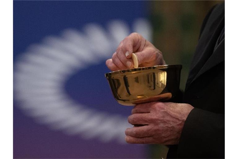 Ein Mitglied der Kirchengemeinde hält während eines Gottesdienstes mit Abendmahl im katholischen Dom St. Bartholomäus vor dem Logo des ÖKT eine Oblate in der Hand. Foto: Sebastian Gollnow/dpa