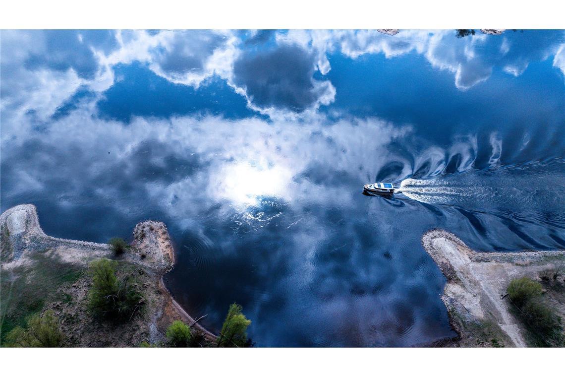 Bilder des Tages Ein Motorboot fährt über die Elbe in deren Wasseroberfläche sich die Wolken spiegeln.