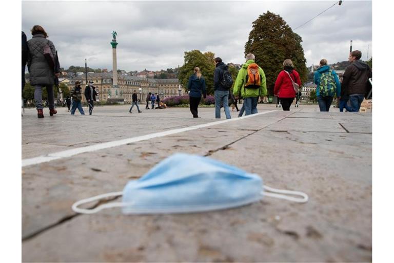Ein Mundschutz liegt auf dem Stuttgarter Schlossplatz auf dem Boden, dahinter zahlreiche Passanten. Foto: Tom Weller/dpa/Archivbild