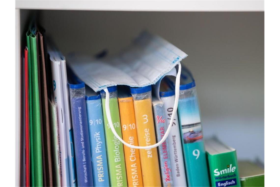 Überwiegende Zahl der Schulen trotz Corona in Betrieb Ein Mundschutz liegt in einem Klassenzimmer auf Schulbüchern. Foto: Marijan Murat/dpa/Archivbild