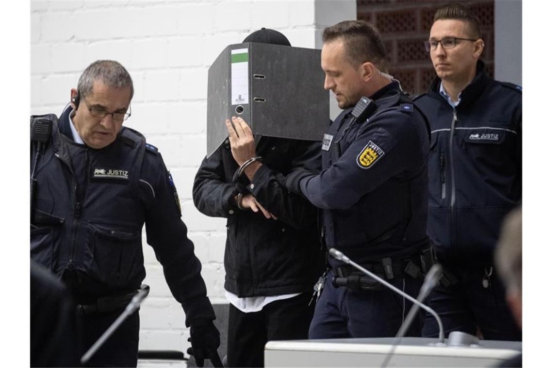 Urteil im Prozess um möglichen Anschlag auf Eisbahn Ein mutmaßlicher Islamist (m) hält sich im Gerichtssaal des Oberlandesgerichtes einen Ordner vor das Gesicht und wird von Justizbeamten an seinen Platz geführt. Dem Deutschen werden Unterstützung und Mitgliedschaft in der Terrormiliz Islamischer Staat vorgeworfen. Foto: Marijan Murat/dpa/Archiv