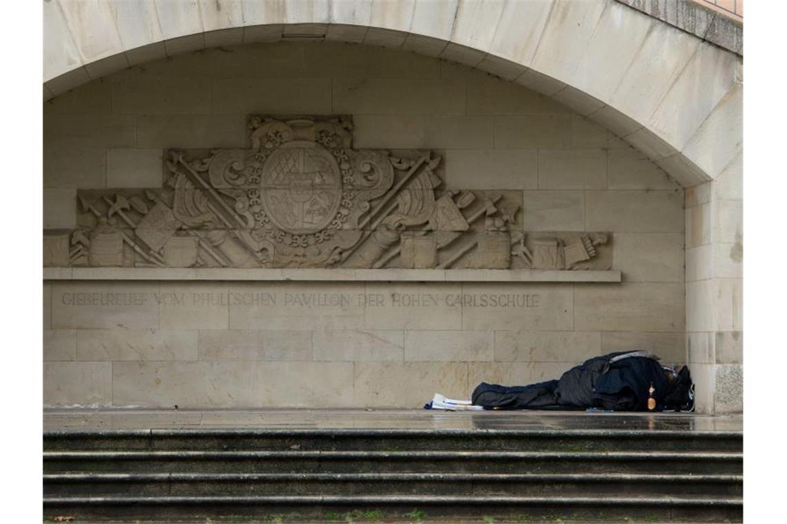 Ein Obdachloser liegt auf der Rückseite des Neuen Schlosses unter dem Giebelrelief der Hohen Karlsschule. Foto: Sebastian Kahnert/Achivbild