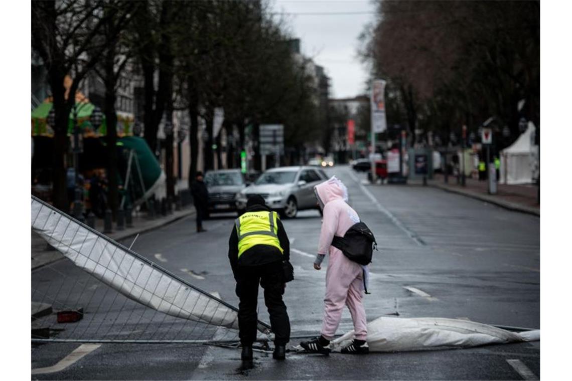 Ein Ordner und ein verkleideter Narr stehen in Düsseldorf an einem Bauzaun, der durch den Sturm umgeweht worden ist. Foto: Fabian Strauch/dpa