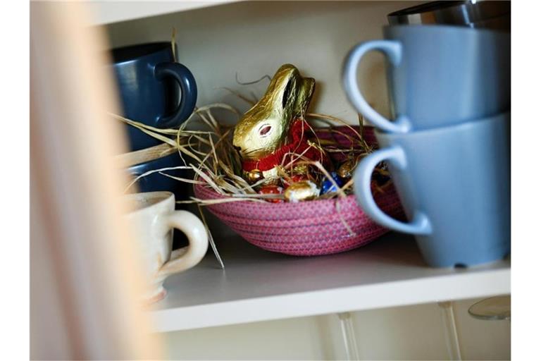 Ein Osternest mit Schokohase und Schokoladeneiern ist in einer Wohnung zwischen Geschirr im Schrank versteckt. Foto: Angelika Warmuth/dpa
